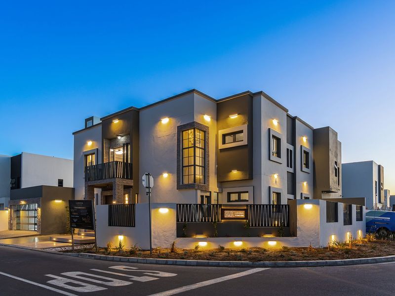 A modern multi-story residential building featuring contemporary architectural design, integrated exterior lighting, a private balcony, and a secure perimeter wall at dusk.