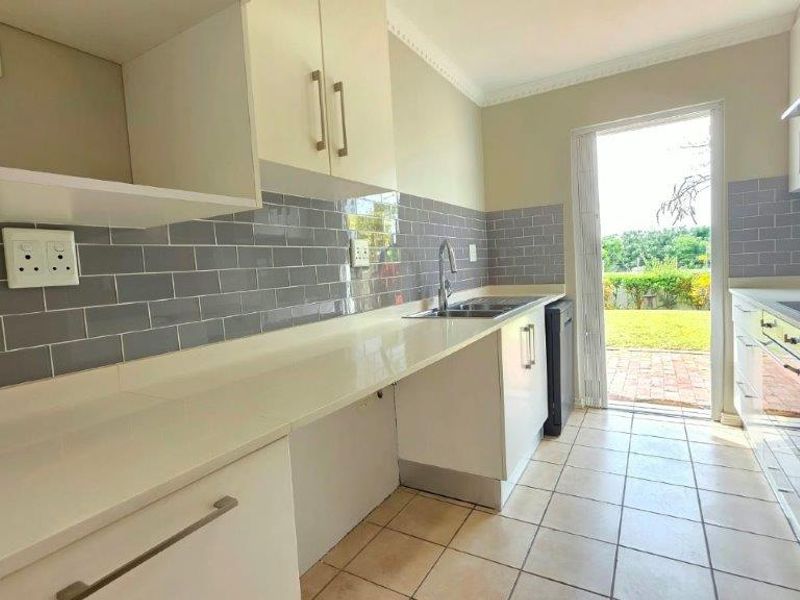 A clean, modern kitchen featuring subway tile backsplash, quartz countertops, built-in appliances, and direct access to the rear garden area.