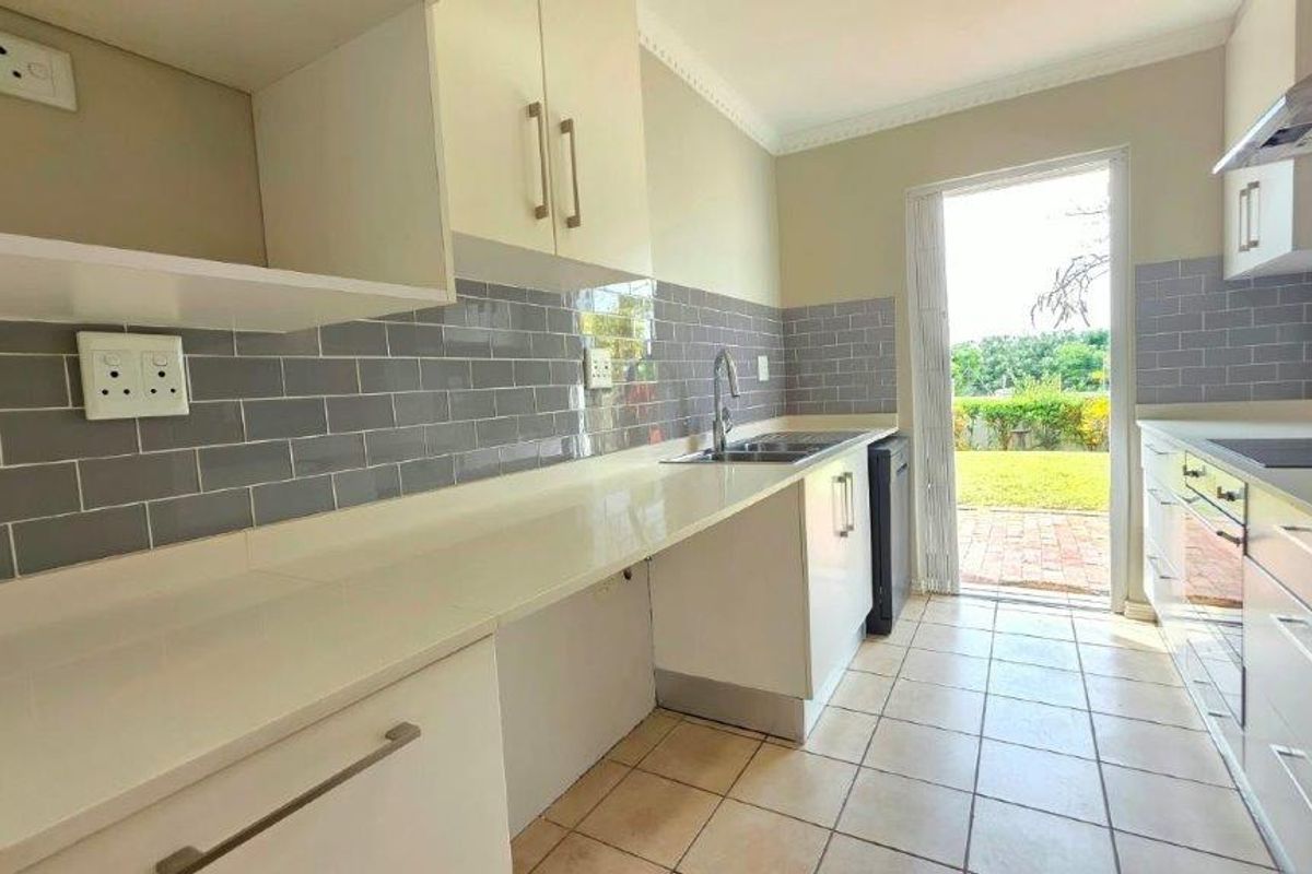 A clean, modern kitchen featuring subway tile backsplash, quartz countertops, built-in appliances, and direct access to the rear garden area.