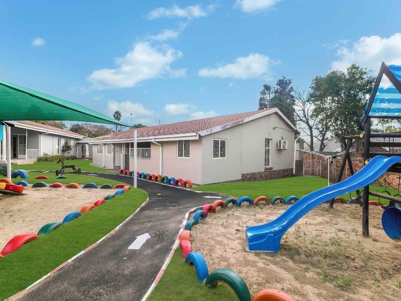 Exterior view of a property featuring a landscaped garden area with a paved pathway, sandpit, and playground equipment.