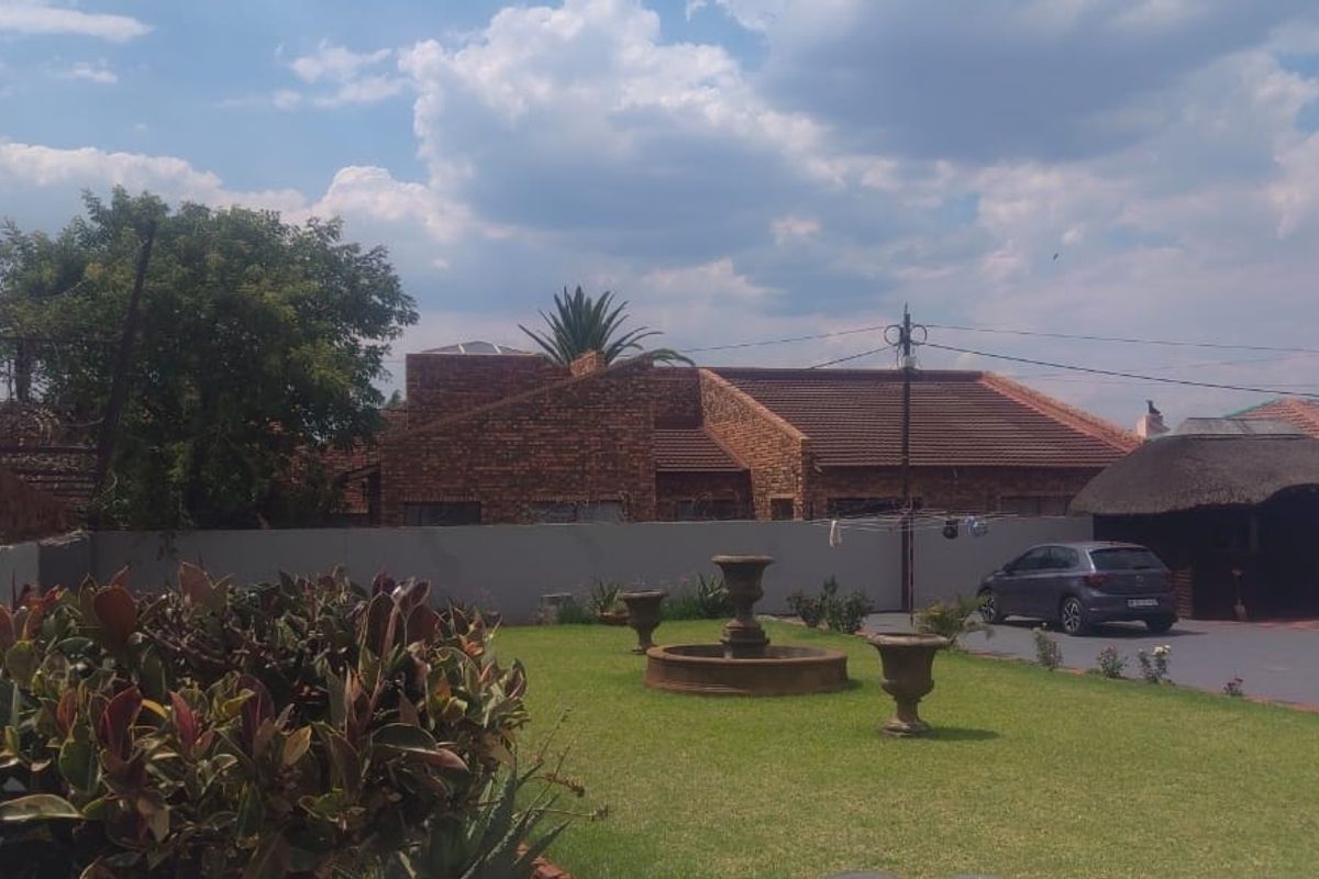A view of the rear garden area featuring a lawn, a decorative stone fountain, and a thatched lapa structure.
