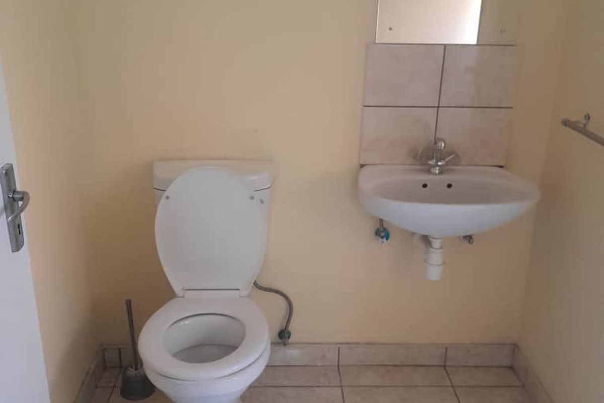 A functional guest bathroom featuring a standard toilet, wall-mounted basin with a mirror, and tiled flooring.