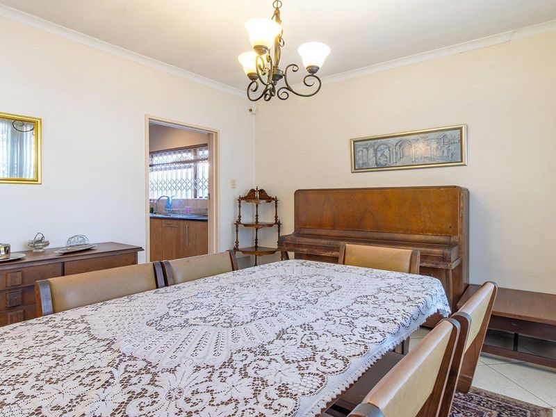 A traditional dining room featuring tiled flooring, a decorative chandelier, and coved cornicing, with an open doorway leading to the kitchen area.