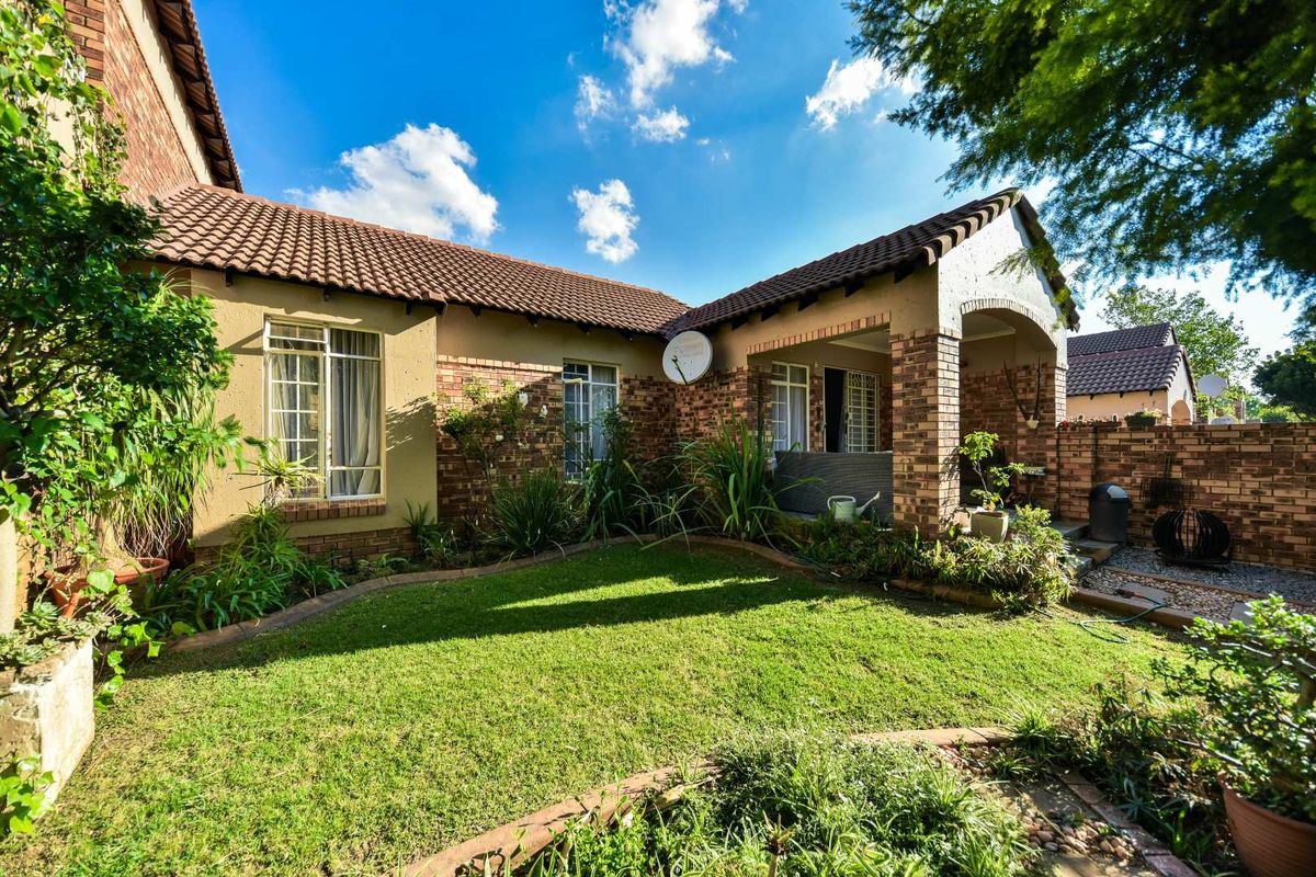 A well-maintained rear exterior view of the townhouse featuring a brick facade, tiled roof, covered patio area, and a private landscaped garden.