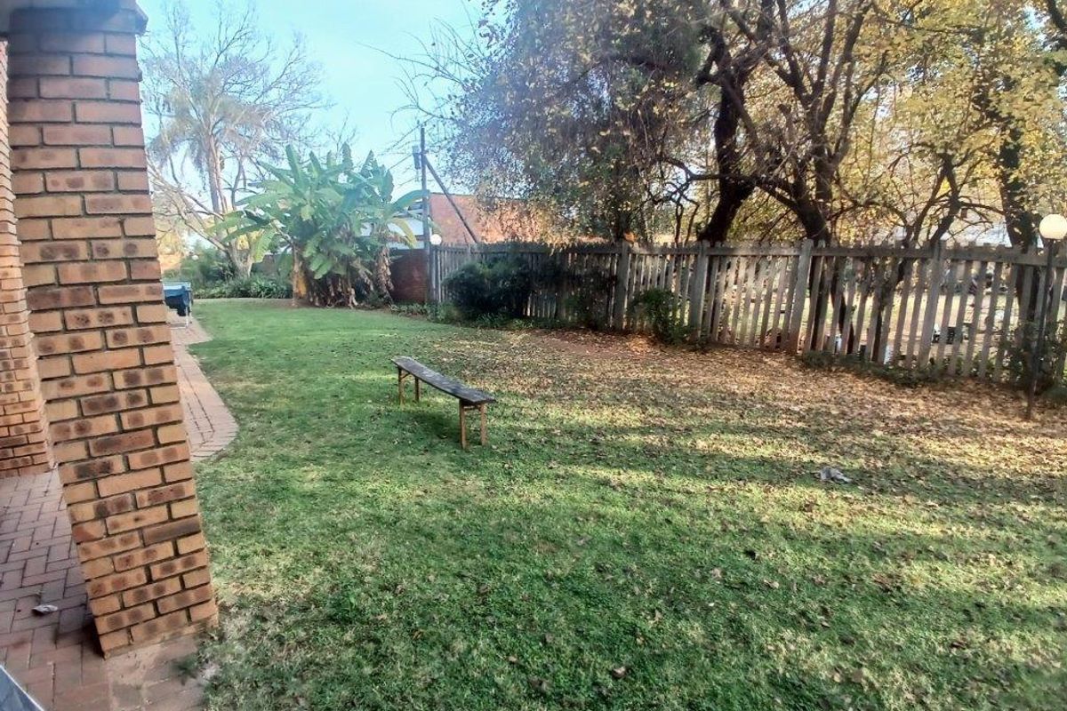 A private rear garden featuring a paved walkway, established lawn, and a wooden picket fence boundary.