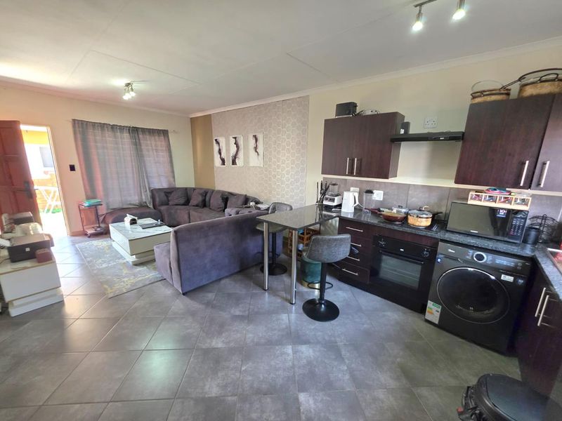 Open-plan living area featuring a kitchen with dark cabinetry, built-in oven, breakfast counter, and tiled flooring, seamlessly connected to the lounge space.