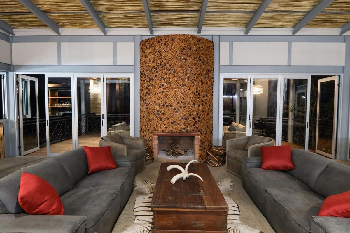 Spacious living area featuring a unique decorative wood-log fireplace surround, exposed beam ceiling with thatch detailing, and large glass sliding doors.