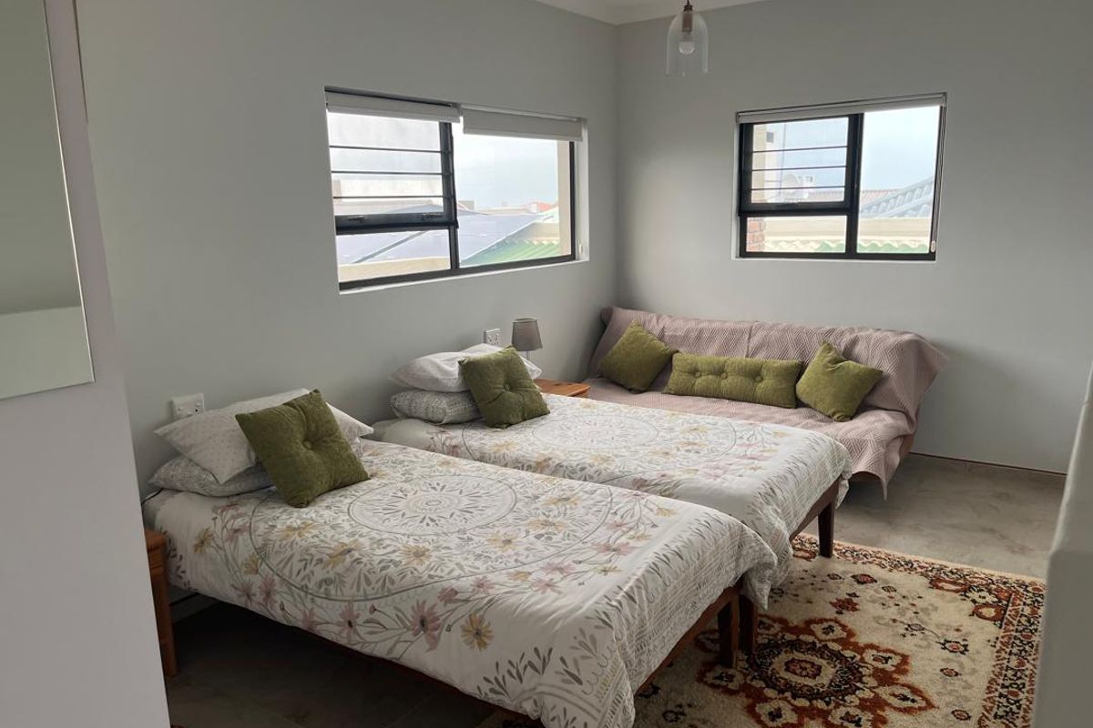 A well-lit bedroom featuring tiled flooring, neutral wall finishes, and aluminium-framed windows with security bars.