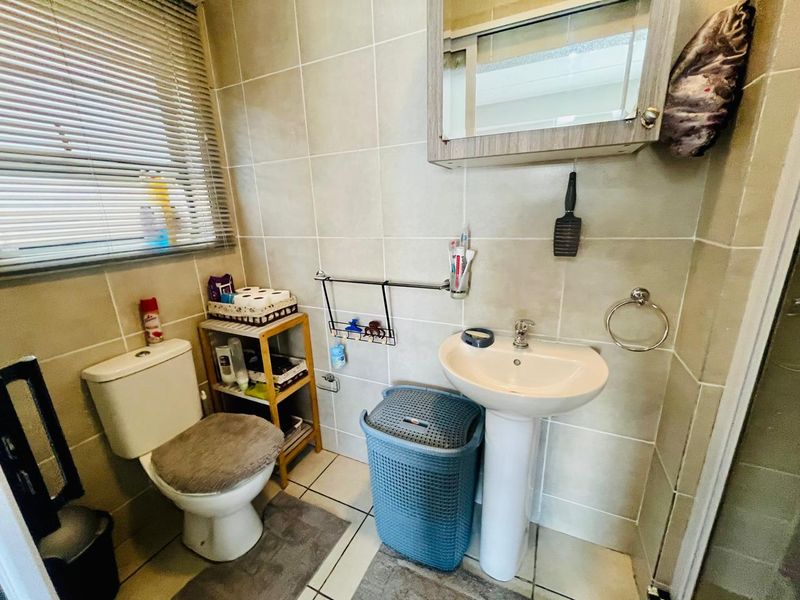 A functional bathroom featuring a pedestal basin, toilet, and tiled finishes, complete with a wall-mounted medicine cabinet and window blinds.