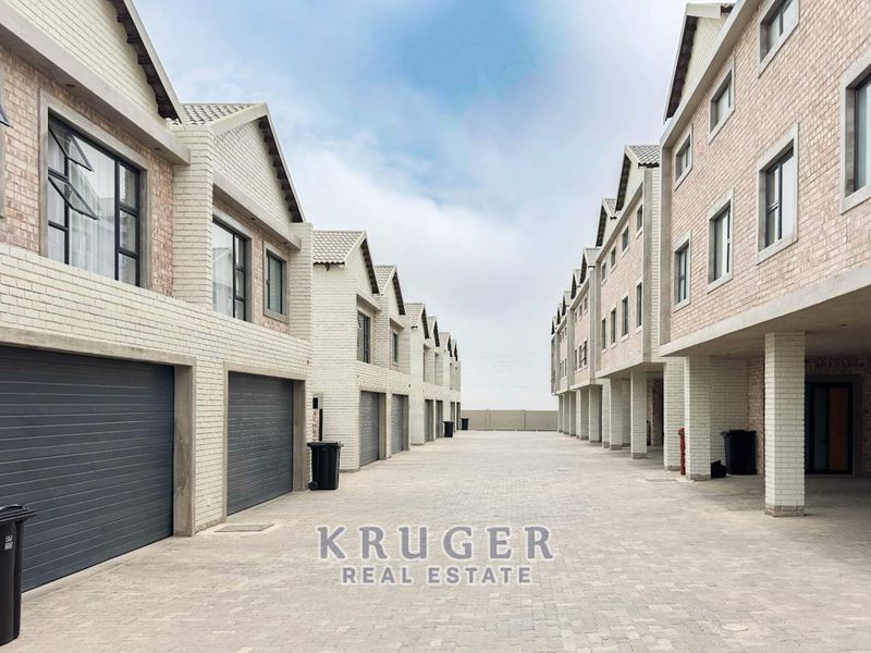 A view of the townhouse complex driveway featuring multiple garage entrances, brick facade construction, and paved common area.