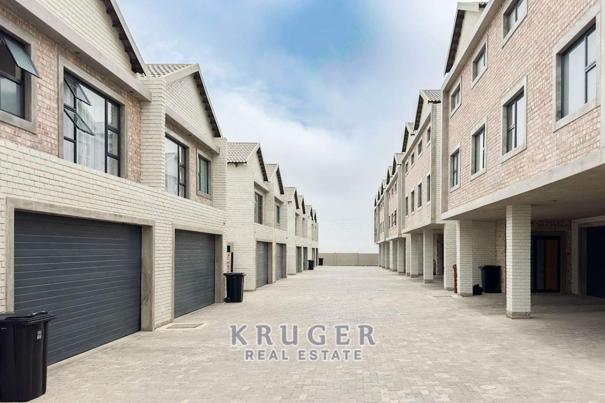 A view of the townhouse complex driveway featuring multiple garage entrances, brick facade construction, and paved common area.