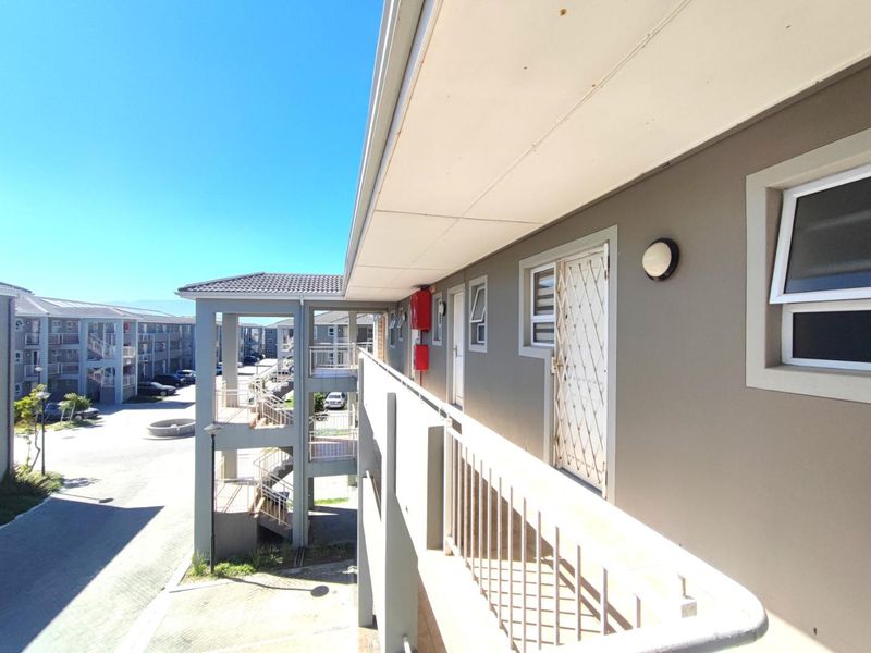 Exterior view of an apartment complex walkway featuring metal security gates, railings, and paved common areas under a clear sky.
