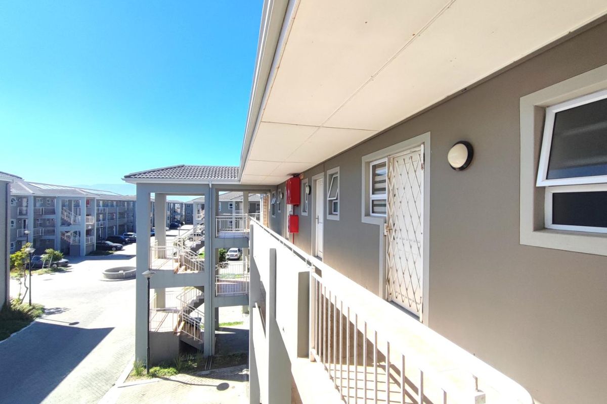 Exterior view of an apartment complex walkway featuring metal security gates, railings, and paved common areas under a clear sky.