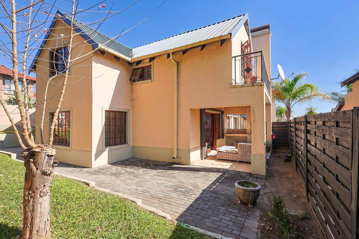Rear view of the property featuring a paved patio area, built-in braai, and an upper-level balcony with a private garden space.