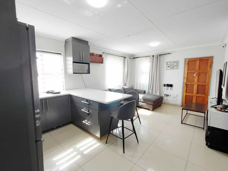An open-plan living and kitchen area featuring modern grey cabinetry, a central island, tiled flooring, and direct access to the main entrance.