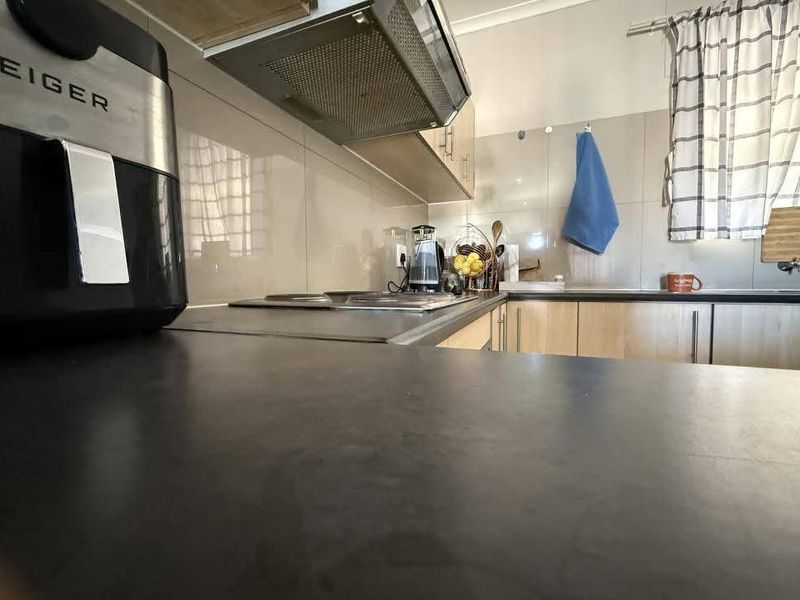 A functional kitchen featuring laminate cabinetry, a built-in hob, an extractor fan, and tiled splashbacks with a dark countertop.