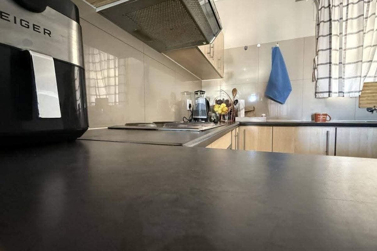 A functional kitchen featuring laminate cabinetry, a built-in hob, an extractor fan, and tiled splashbacks with a dark countertop.