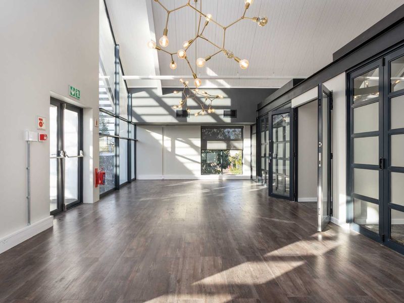 A bright, modern open-plan office space featuring high ceilings, large windows, contemporary lighting, and high-quality laminate flooring.