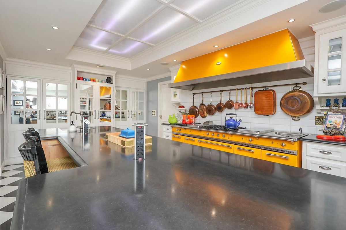 Spacious gourmet kitchen featuring a large central island, professional-grade yellow range cooker, custom hood, and elegant glass-front cabinetry with high-end finishes.