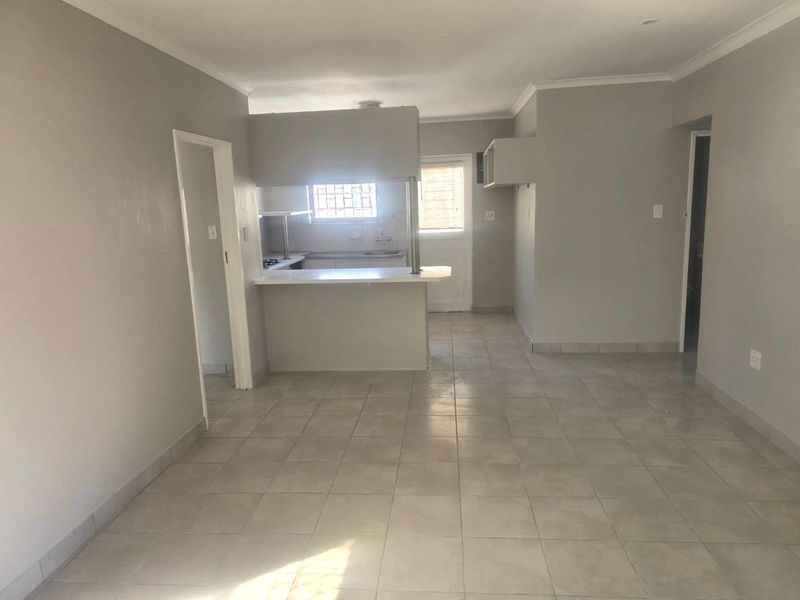 An open-plan living and kitchen area featuring neutral tiled flooring, a breakfast bar, and functional kitchen cabinetry.