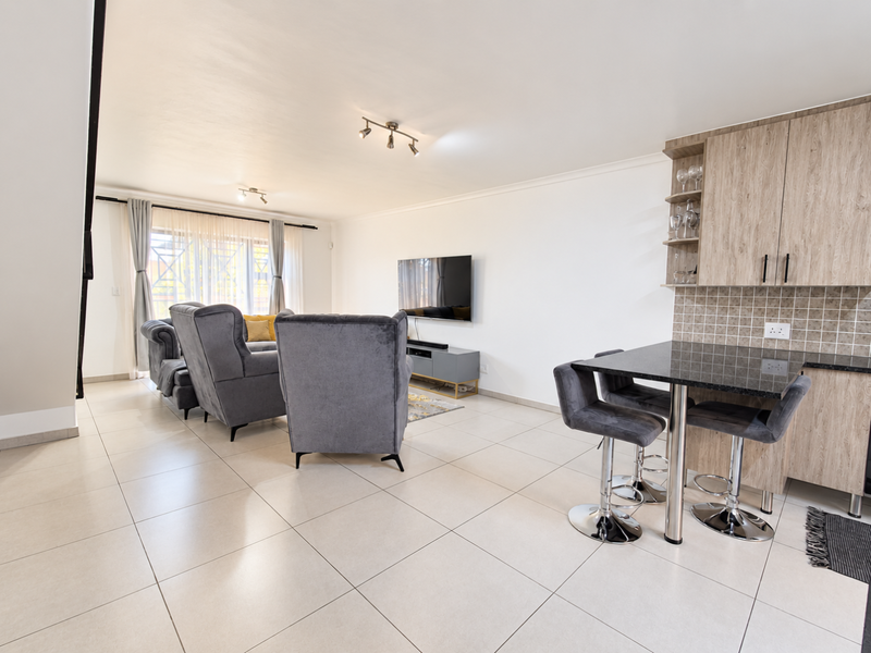 Spacious open-plan living area featuring large format floor tiles, a modern kitchen breakfast bar with granite countertops, and integrated cabinetry.