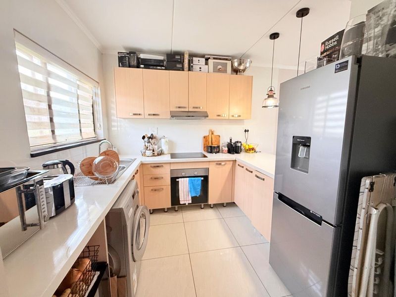 A functional U-shaped kitchen featuring light wood cabinetry, integrated appliances, tiled flooring, and ample counter space for meal preparation.