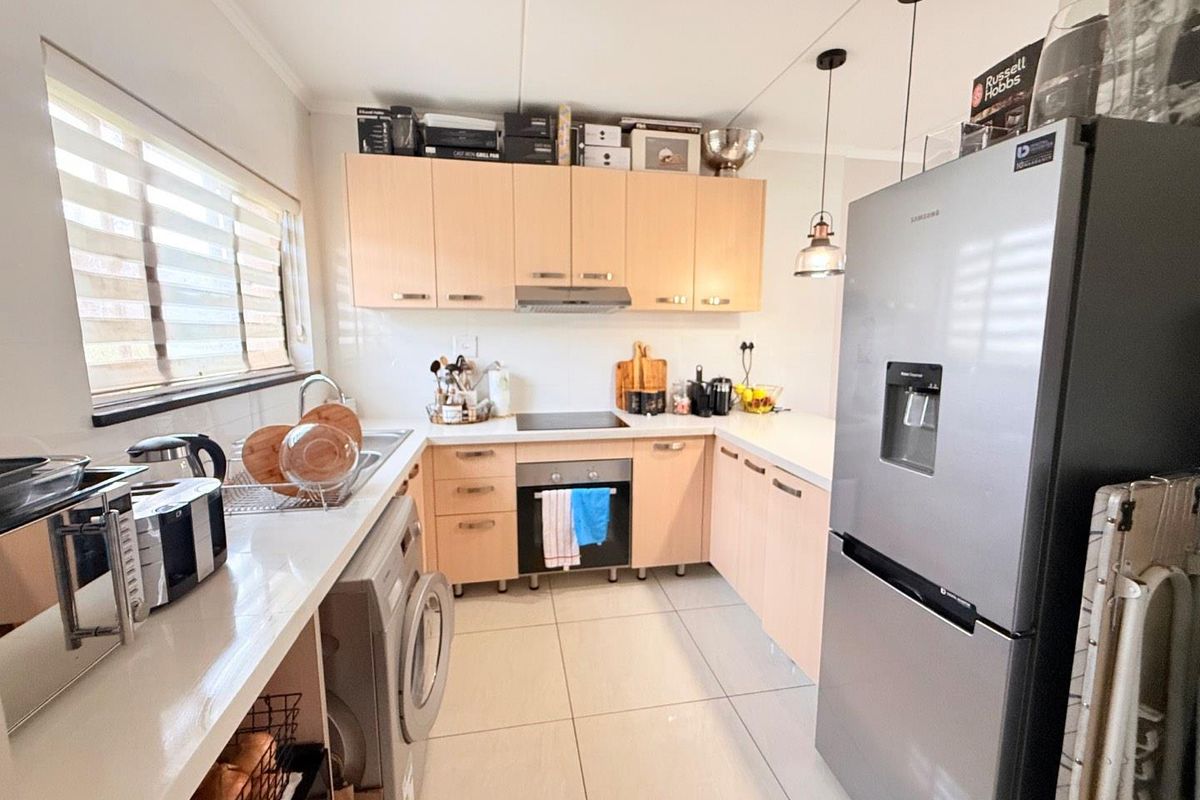 A functional U-shaped kitchen featuring light wood cabinetry, integrated appliances, tiled flooring, and ample counter space for meal preparation.