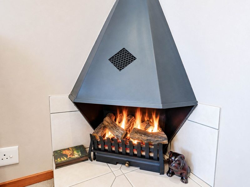 A modern, corner-mounted built-in fireplace with a sleek metal hood and tiled hearth, providing a functional and aesthetic focal point for the living area.