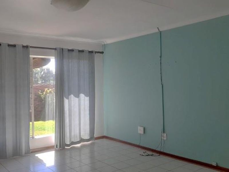 An empty living room featuring tiled flooring, a sliding glass door providing natural light, and a feature wall with exposed surface-mounted electrical wiring.