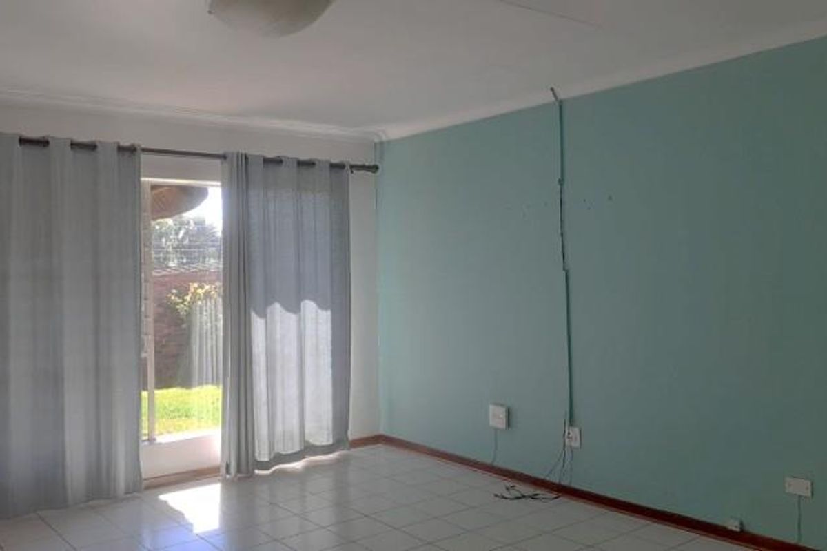An empty living room featuring tiled flooring, a sliding glass door providing natural light, and a feature wall with exposed surface-mounted electrical wiring.