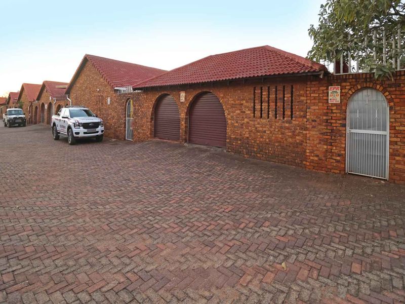 Exterior view of a townhouse complex featuring brick facades, tiled roofs, and multiple roller garage doors along a paved driveway.