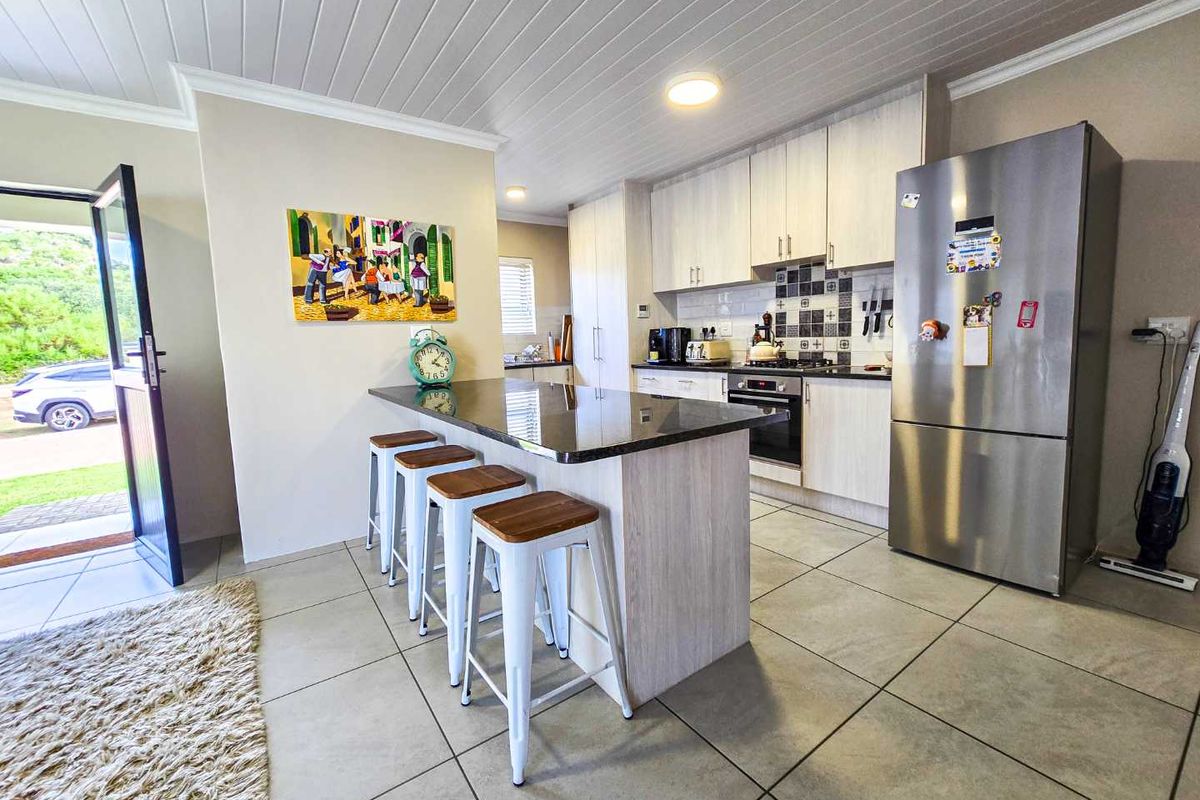 Modern kitchen featuring a central island with stone countertop, light wood cabinetry, tiled flooring, and integrated oven and hob.