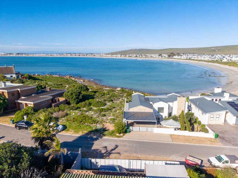 Aerial view of a coastal property featuring a metal roof, stone facade, and carport, situated directly along the beachfront.