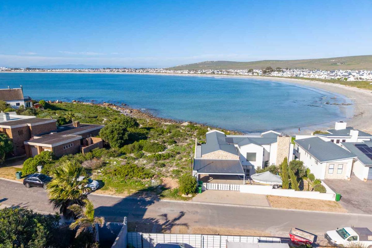 Aerial view of a coastal property featuring a metal roof, stone facade, and carport, situated directly along the beachfront.