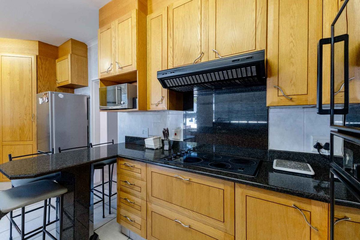 A functional kitchen featuring wooden cabinetry, granite countertops, an electric hob with extractor fan, and a convenient breakfast bar for casual dining.