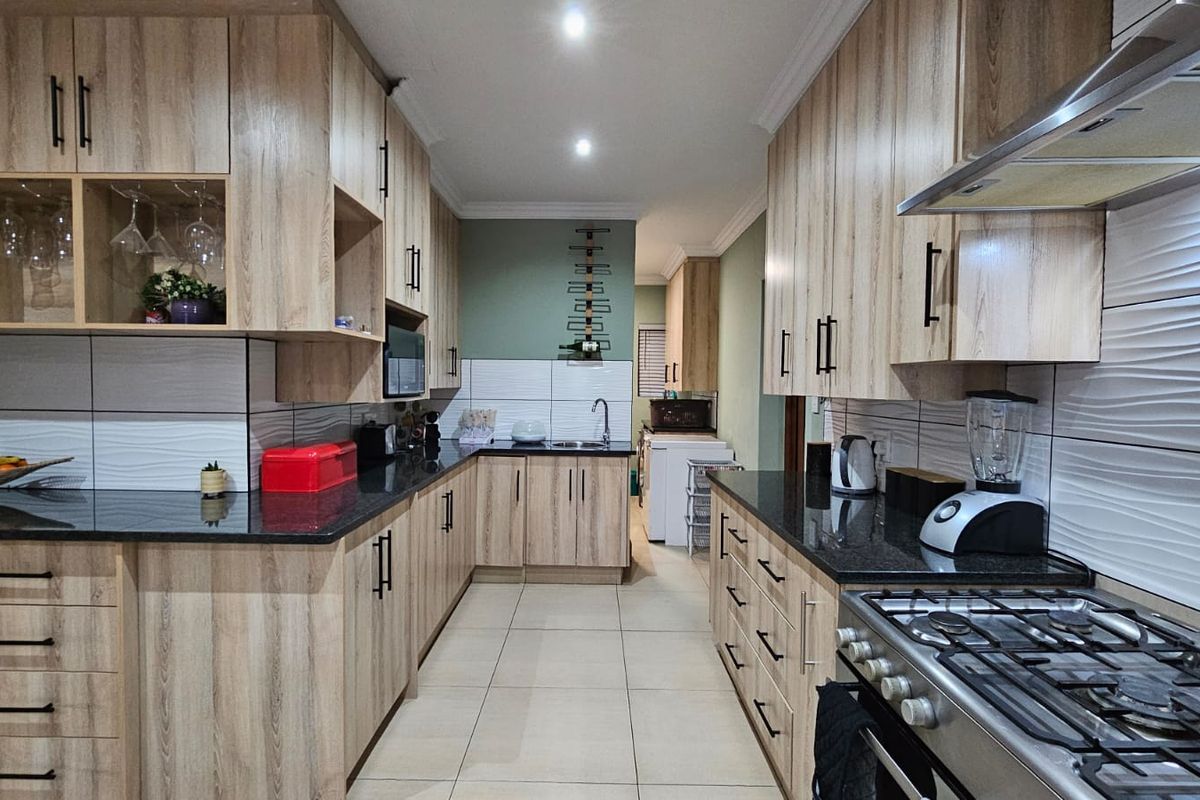 Modern kitchen featuring light wood-grain cabinetry, dark granite countertops, gas stove with extractor, and contemporary textured wall tiling.