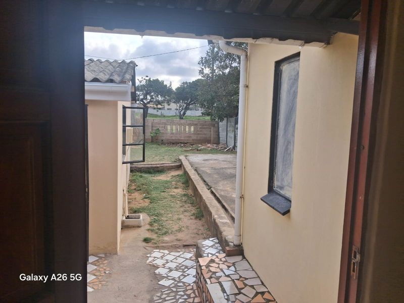 A view of the rear exterior area featuring a concrete pathway, tiled step, and boundary wall, showing signs of wear and requiring maintenance.