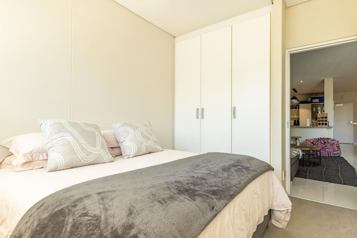 A well-maintained bedroom featuring built-in cupboards and neutral finishes, with a view through to the adjacent living area.