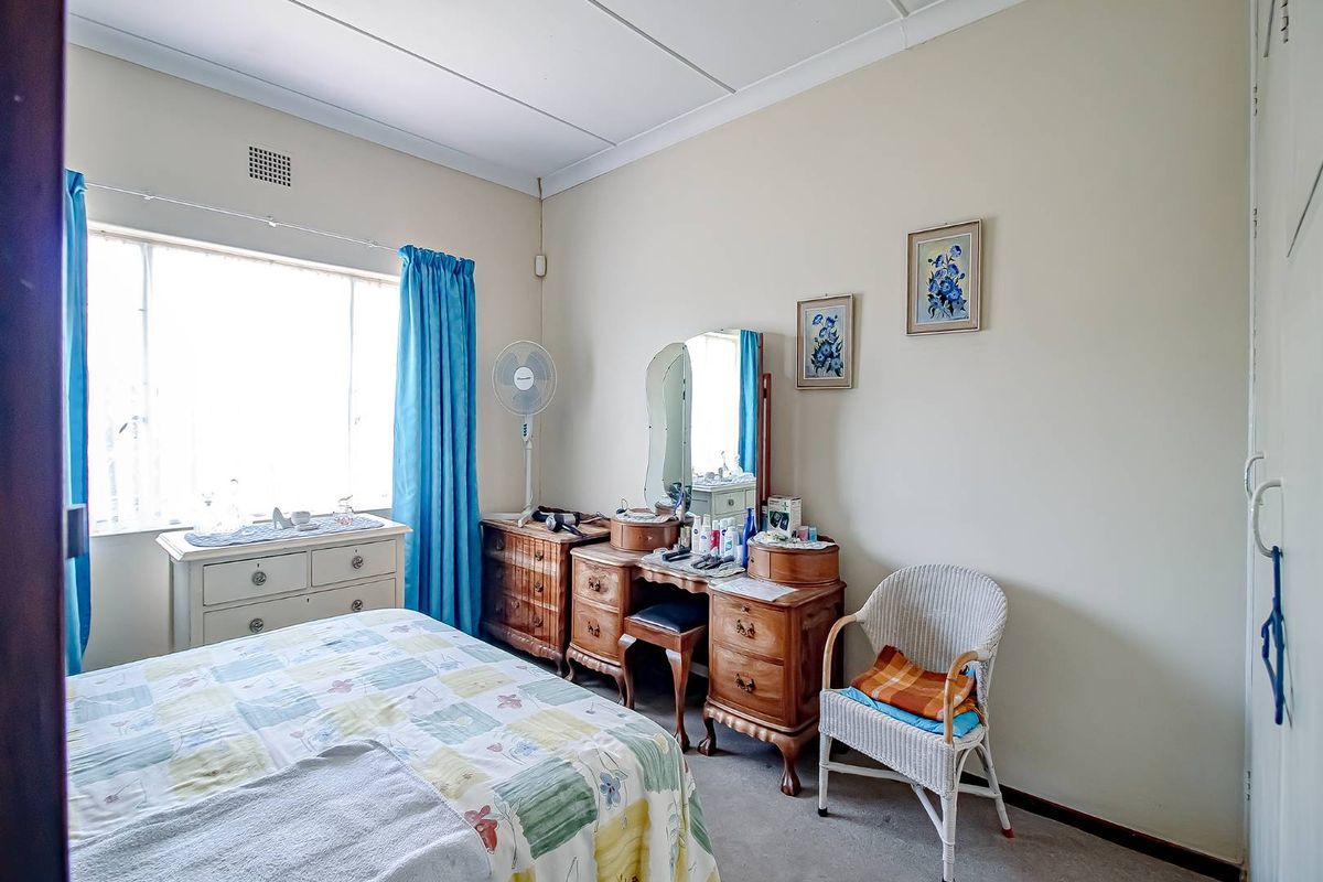 A functional bedroom featuring a large window, neutral wall tones, and carpeted flooring, offering a comfortable and well-lit living space.