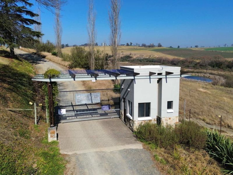 Aerial view of a secure residential estate entrance featuring a gated access point, guard house, and solar panel installation.