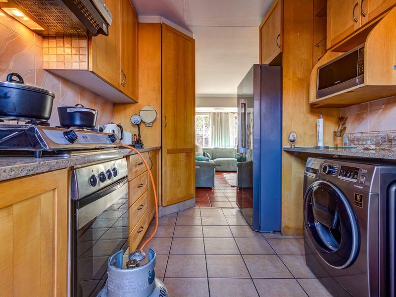 A functional kitchen featuring wooden cabinetry, granite countertops, a gas stove with extractor, and tiled finishes, leading into an adjacent living area.