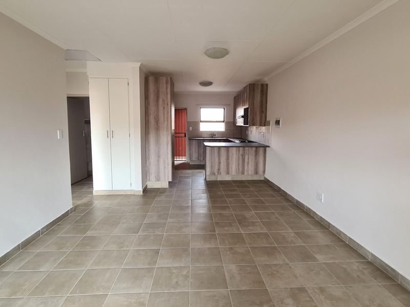 An open-plan living and kitchen area featuring neutral tiled flooring, built-in cabinetry, and a functional layout in a well-maintained apartment.