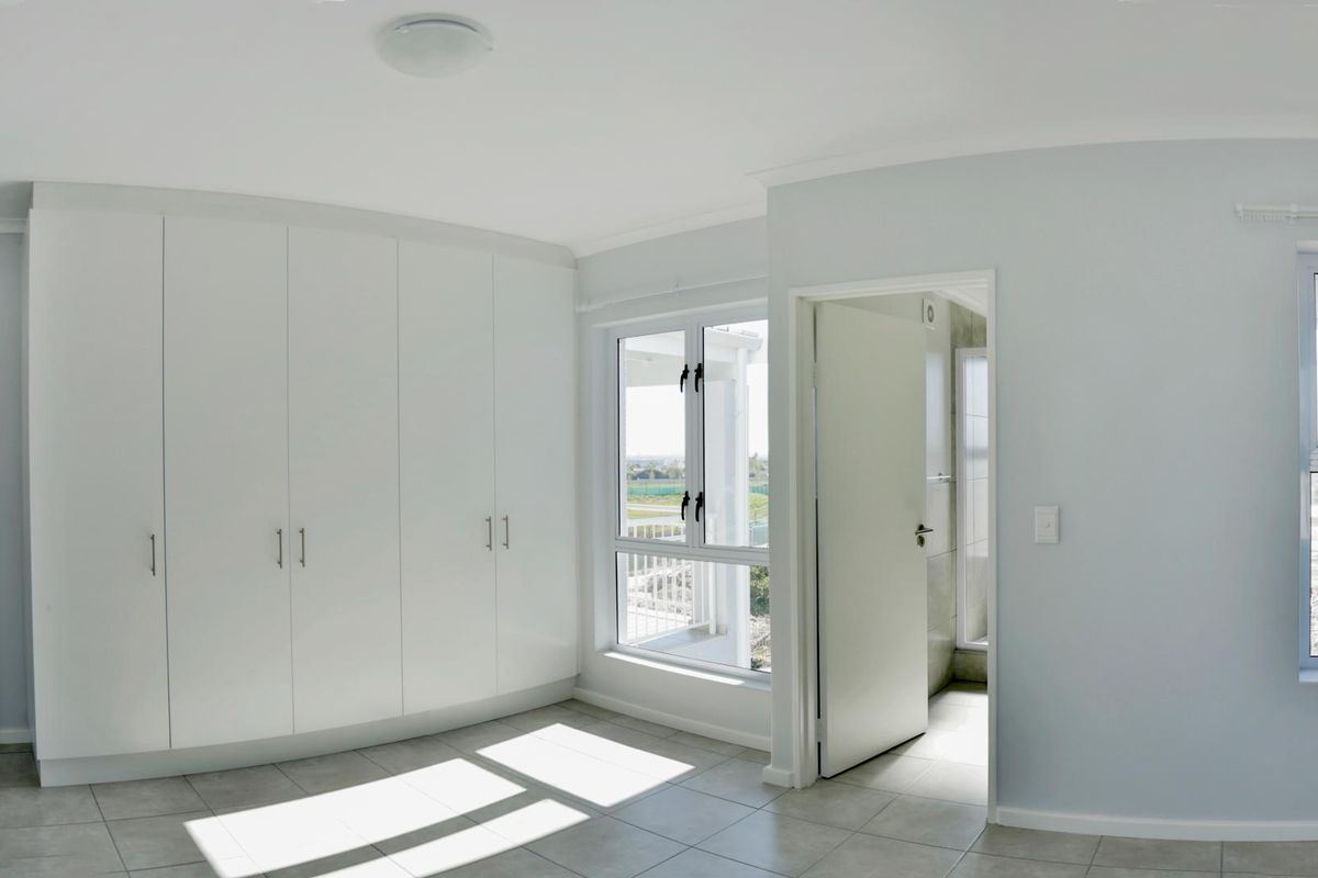 A bright, modern bedroom featuring built-in floor-to-ceiling wardrobes, tiled flooring, and an en-suite bathroom entrance.
