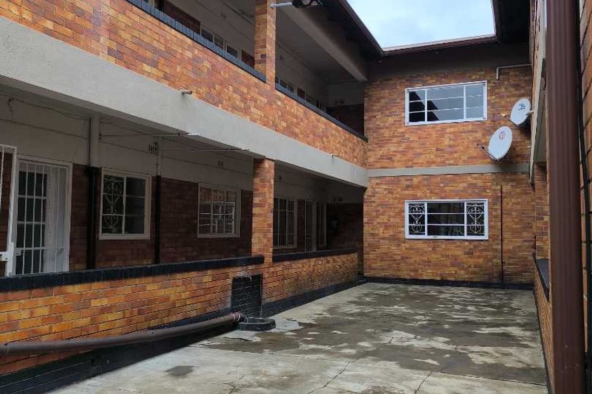Exterior view of an apartment complex courtyard featuring brick facade, concrete flooring, and metal security window grilles.