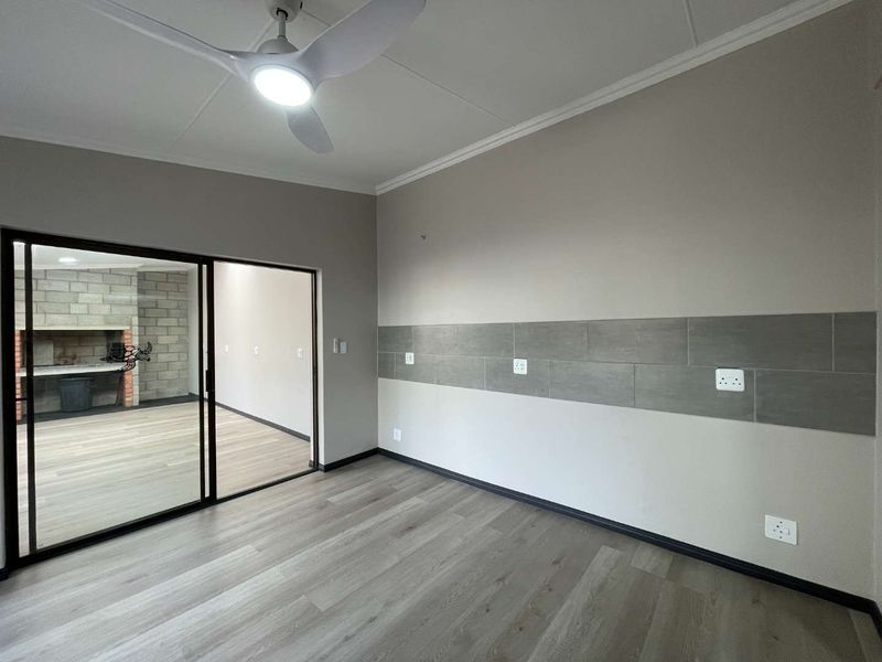 A bright, empty living area featuring modern laminate flooring, a ceiling fan, and a sliding glass door leading to an outdoor space.