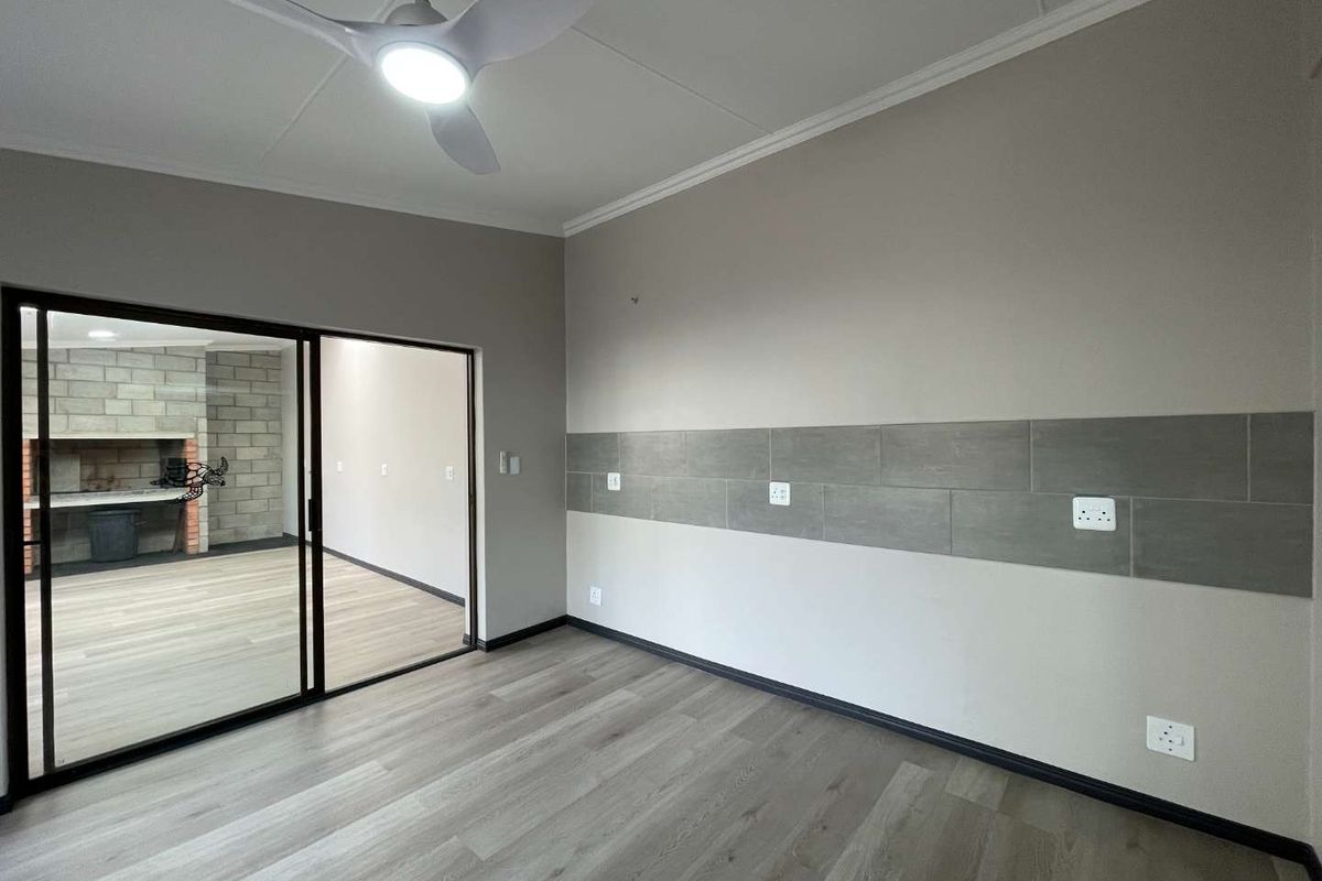 A bright, empty living area featuring modern laminate flooring, a ceiling fan, and a sliding glass door leading to an outdoor space.