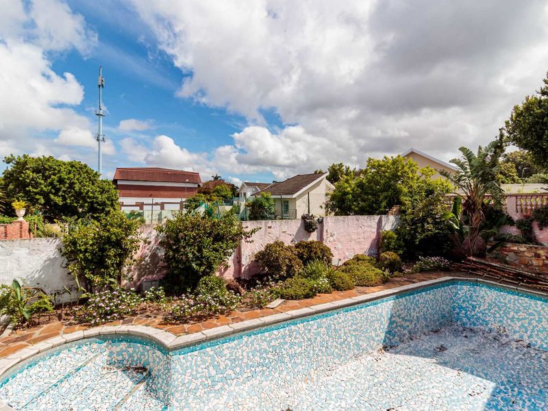 Outdoor pool area featuring a tiled swimming pool, stone paving, and perimeter boundary walls in need of maintenance.