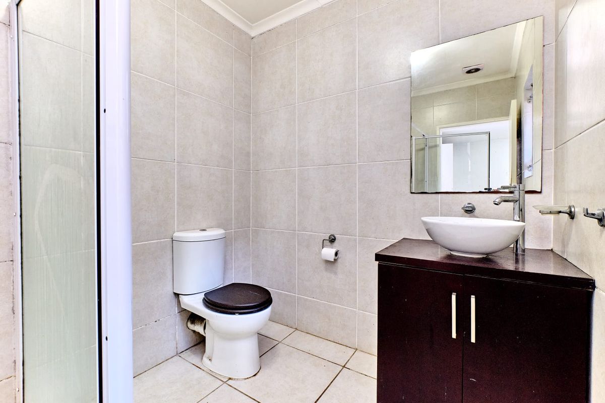A compact bathroom featuring neutral wall and floor tiles, a modern vessel sink on a dark wood vanity, and a wall-mounted mirror.