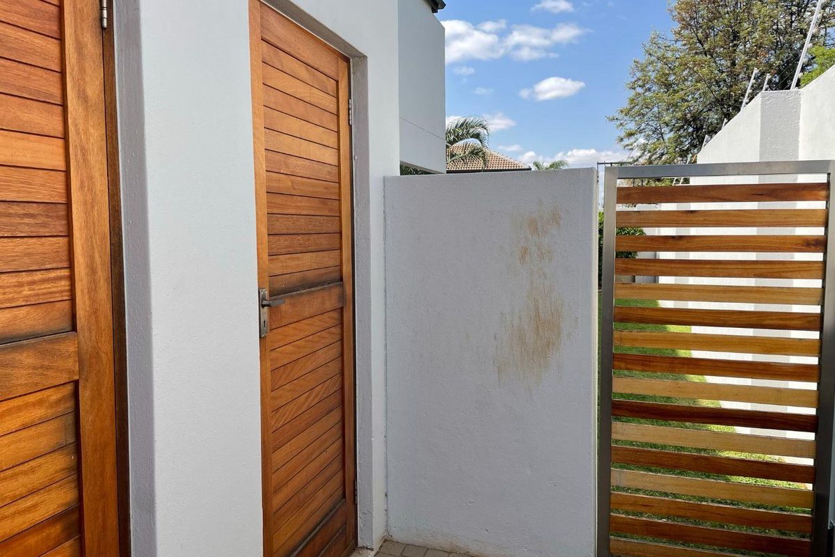 Exterior view of a private entrance area featuring timber slat doors and a matching privacy screen with paved flooring.