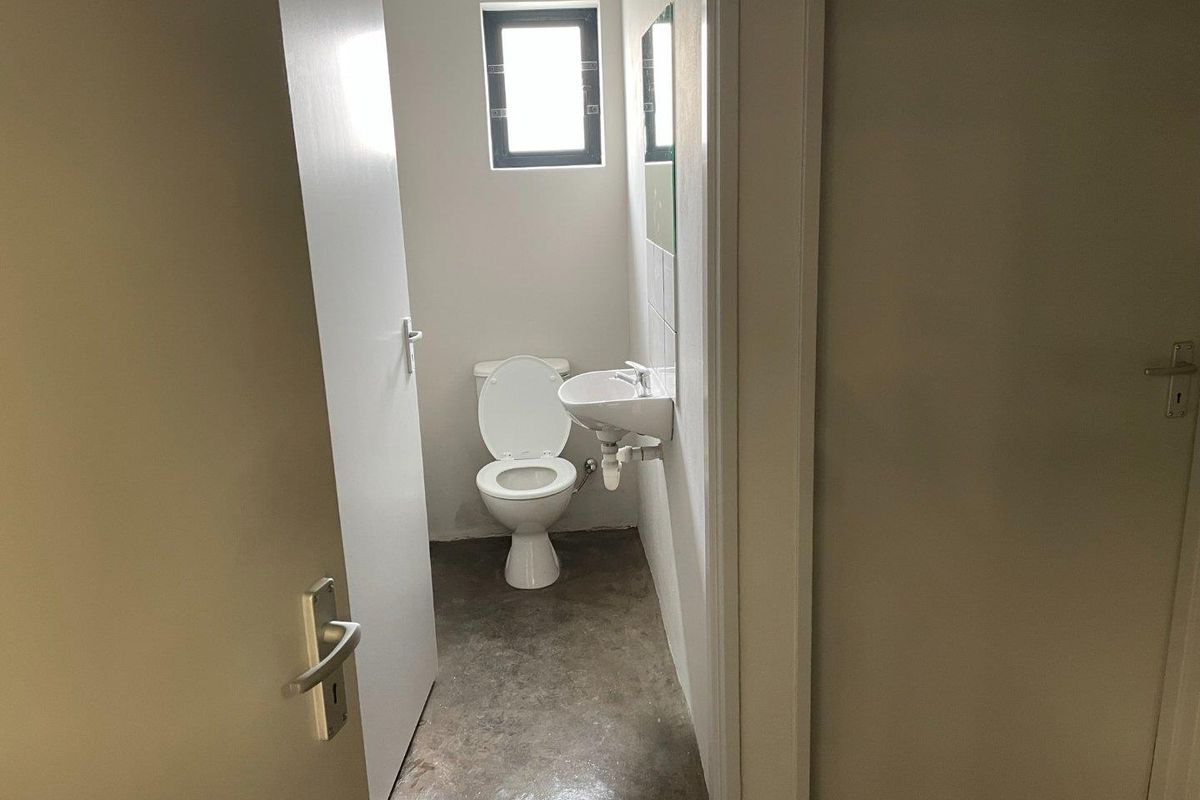 A compact industrial-style restroom featuring a wall-mounted basin, a standard toilet, and polished concrete flooring.
